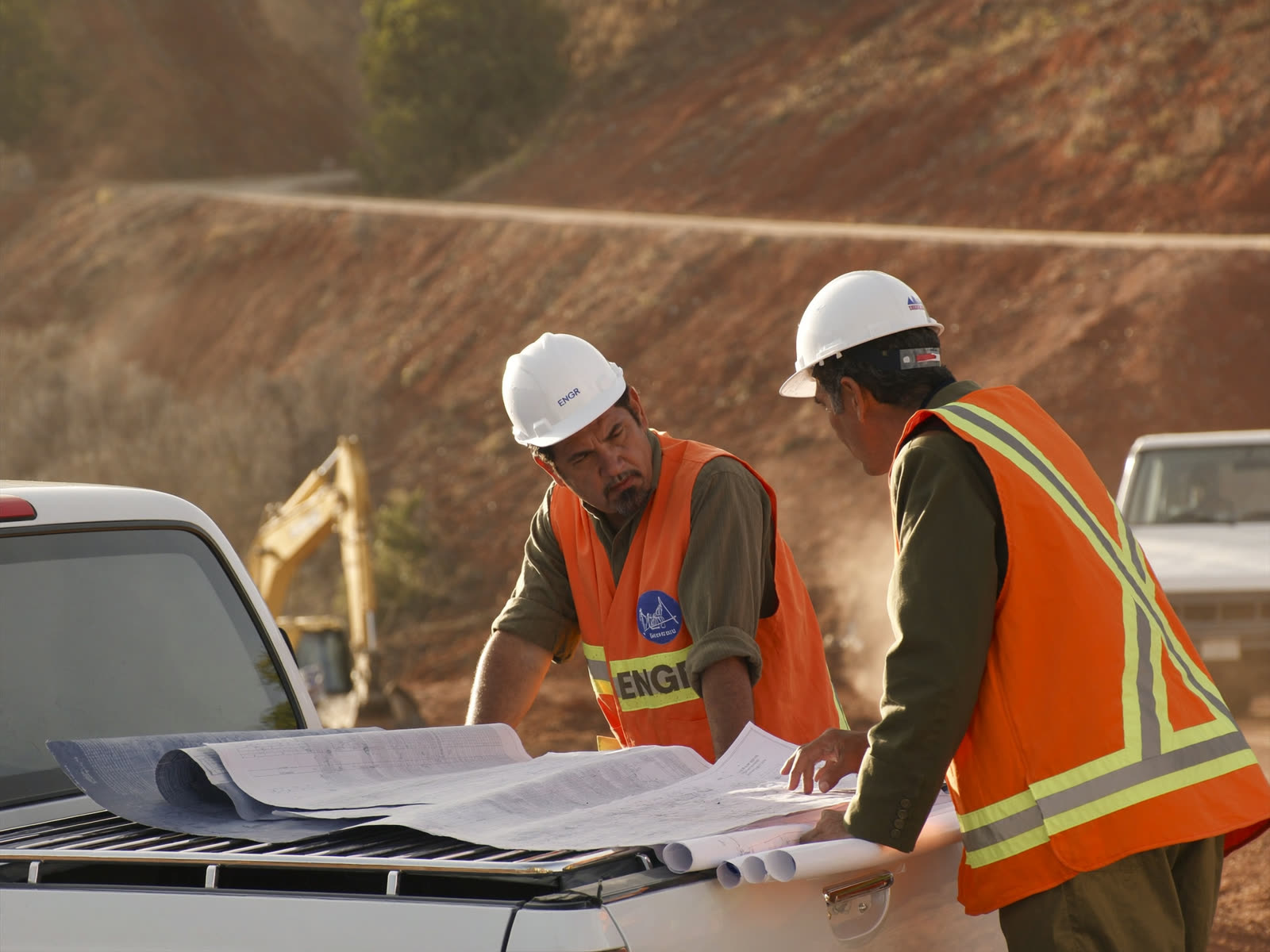 Ingenieros revisando planos de obra en campo junto a maquinaria